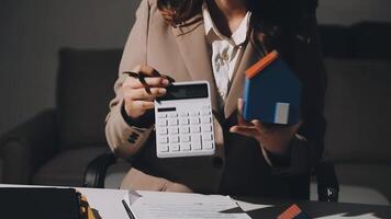 A woman in a business suit is holding a calculator and a house model video