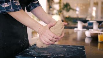 Female hands crumple and roll out piece of clay on table. Potter prepares clay for processing on table. video