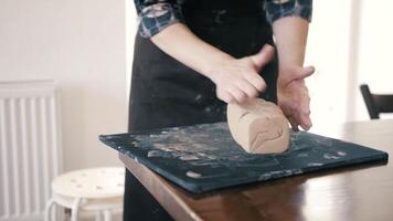 Female hands crumple and roll out piece of clay on table, front view, closeup. Potter prepares clay for processing on table video
