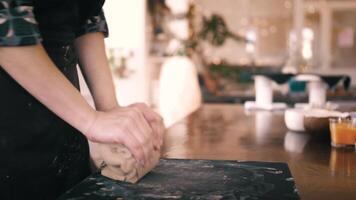 Female hands crumple and roll out piece of clay on table,, closeup. Potter prepares clay for processing on table. video