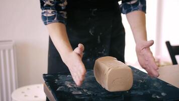Female hands crumple and roll out piece of clay on table, front view. Potter prepares clay for processing on table. video