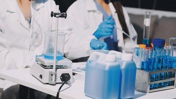 Two people in lab coats working on a table with blue liquid video