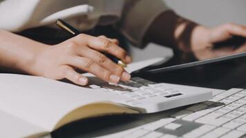 A woman's hands are on a calculator and pen while using a laptop video