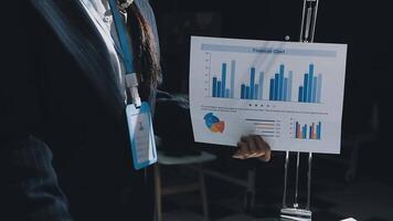 A person in a suit holding a piece of paper with graphs video