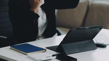 A woman in a business suit is sitting at a desk with a laptop and a tablet video