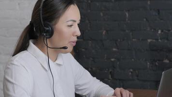 Customer service representative in headset communicating via laptop, engaged in support or virtual assistance in modern office setting. 18 video