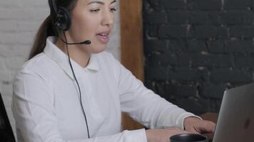 Customer service representative in headset communicating via laptop, engaged in support or virtual assistance in modern office setting. 15 video