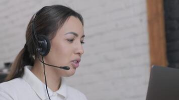 Customer service representative in headset communicating via laptop, engaged in support or virtual assistance in modern office setting. video