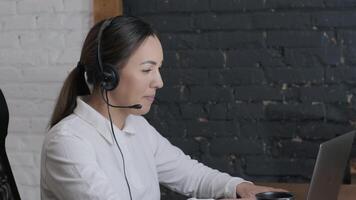 Customer service representative in headset communicating via laptop, engaged in support or virtual assistance in modern office setting. 16 video