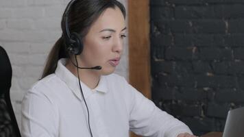 Customer service representative in headset communicating via laptop, engaged in support or virtual assistance in modern office setting. 17 video
