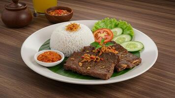 Grilled beef ribs served with sambal, rice, and fresh vegetables on a plate photo