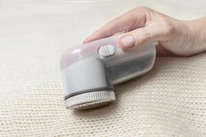 Machine for removing pellets from a woolen white jacket. A hand holds a reel removal machine close up photo
