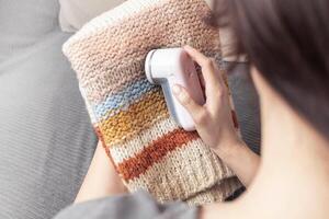 Woman uses a machine for removing pellet and spools from woolly. A modern electronic device for updating old things close up photo