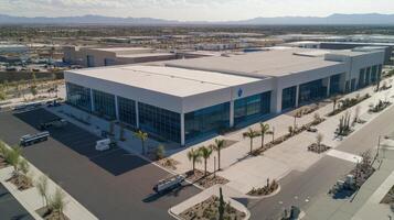 Aerial view of a modern industrial building with a large parking area and desert landscape photo