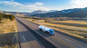 A truck transporting a cylindrical tank on a wide highway surrounded by mountains and fields photo