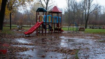 A playground with slides and swings, surrounded by wet ground and fallen leaves on a rainy day photo