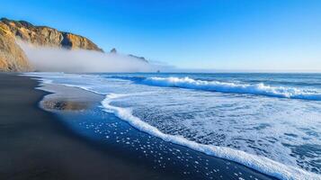A serene beach scene with waves, cliffs, and fog under a clear blue sky. photo