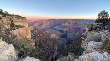 A scenic view of the Grand Canyon at sunset, showcasing layered rock formations and vegetation. photo
