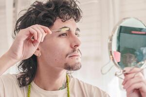 Young man combing eyebrows with a small brush and mirror in bathroom photo