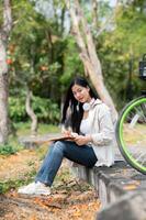 Asian woman is looking straight into camera while writing on her notebook, sitting on park sidewalk. photo