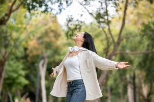 An asian woman is standing with open arms while turning around in the park, breathing in fresh air. photo