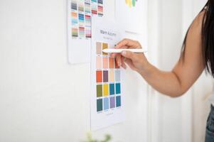 Close up of hand holding a stylus pointing at a color on printed color palette sticking on the wall photo