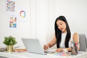An asian woman is looking at the printed color chart while working on the design with graphic tablet. photo