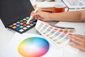 Close up of a hand pointing a stylus at red color on a color palette. Choosing or picking a color. photo
