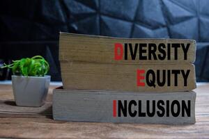 Books with words Diversity Equity Inclusion on wooden table and black background photo