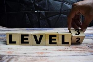 Concept word Time for level 3, hand turns a cube and changes words level 2 to level 3 on wooden blocks on a wooden table photo