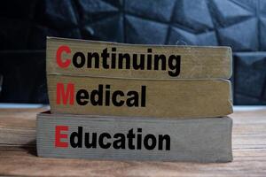 Books with words CME - Continuing Medical Education on wooden table and black background photo