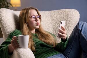 Woman with coffee and smartphone shows surprised expression while reading something online at home. photo