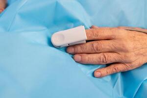 Elderly hand with pulse oximeter clip on finger for oxygen monitoring in medical setting. photo
