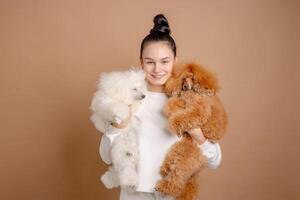 Happy woman in white clothes holding two fluffy poodles in studio with neutral background. photo