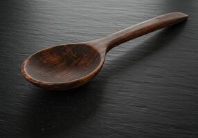Closeup of carved wooden spoon on dark textured background with rustic minimal style showing natural brown color and detailed craftsmanship in studio flatlay shot photo