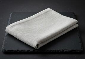 Beige folded linen fabric on dark slate surface with natural textile texture in minimal neutral style flatlay closeup for background or design use photo