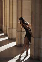 Ballet dancer en pointe leaning gently on column in sunlit stone corridor photo