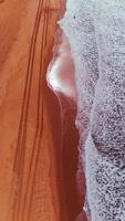 Overhead Drone View of Ocean Waves and Tire Tracks on Red-Toned Beach photo