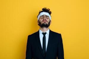 A funny man dressed in a black suit sports a headband bandage while striking a playful pose in front of a vibrant yellow backdrop photo