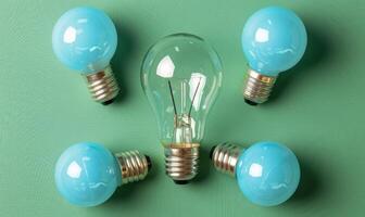 A central clear light bulb shines brightly, bordered by four blue bulbs on a green surface photo
