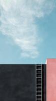A striking architectural setup displays a black wall adjacent to a pink structure, complemented by a blue sky and wispy clouds above photo