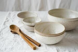 Simple ceramic bowls are artfully displayed alongside wooden spoons on a textured linen backdrop photo