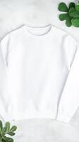 A simple white sweatshirt is neatly arranged on a soft surface, surrounded by fresh green plants, creating a calm atmosphere perfect for relaxation photo