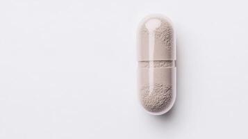 A large capsule containing a fine gray powder lies flat on a smooth white surface, showcasing its interior texture and color clearly photo