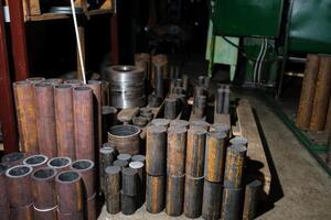 Various metal cylinders and pipes stacked in a workshop setting during daytime in a manufacturing facility photo