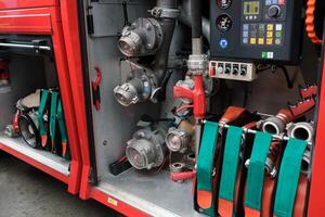 Equipment used for firefighting is neatly organized in a fire truck compartment with hoses, valves, and control panels present in the background during daylight hours photo