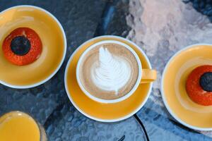 Warm latte art accompanied by two orange desserts on a sunny outdoor table setting during a relaxed afternoon brunch photo