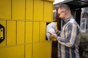 Man retrieving a package from a yellow delivery locker in a busy urban area during daylight hours photo
