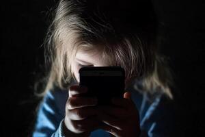 A young girl is holding a cell phone in the dark photo
