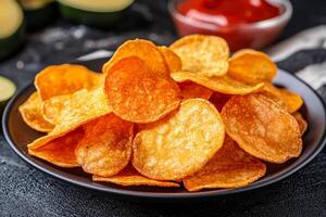 Potato chips in a black bowl on a dark table photo